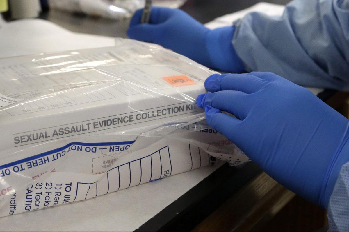 A person's hands wearing blue medical gloves works with a box labeled "sexual assault evidence collection" in a bag.